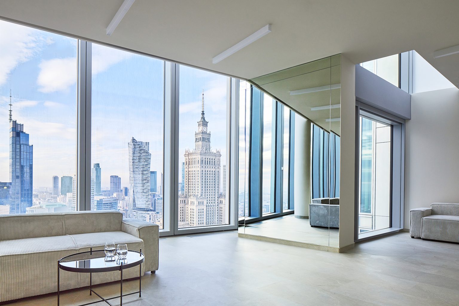 Przeszklony narożnik ze strefą lounge i lustrzaną ścianą, w tle panorama centrum Warszawy
