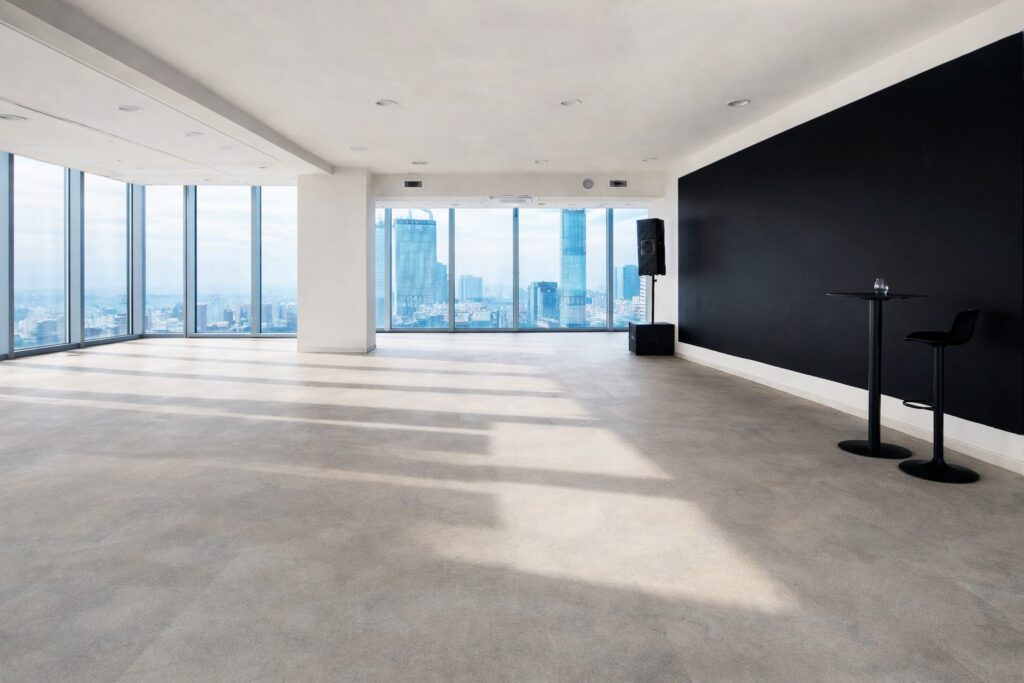 Pusta sala z ciemną ścianą ekranową i stolikiem koktajlowym, panorama Warszawy za oknami